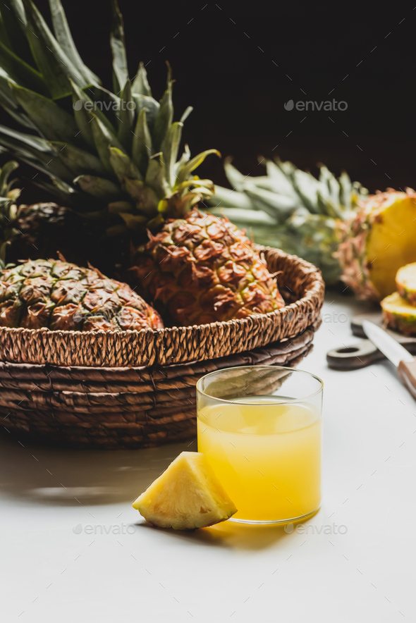 Fresh Pineapple Juice in Glass Near Delicious Fruit in Basket on White Background Isolated on Black
