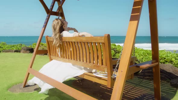 Carefree Woman Swinging at Blue Ocean with Raised Handswind Blowing White Dress alt