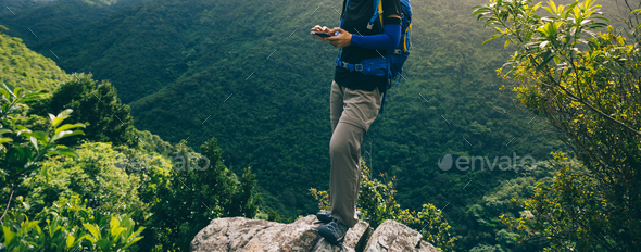 Hiker using smartphone on forest mountain top cliff edge