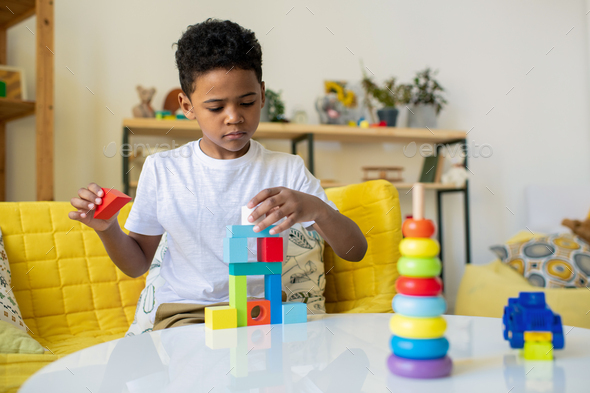 Cute serious boy of elementary age building tower or multi-storey cube house - Stock Photo - Images