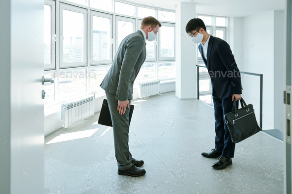 Elegant intercultural businessmen with briefcases greeting each other by bow