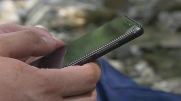 Male Hands Type Text Message on Smartphone on Mountain Stream Background