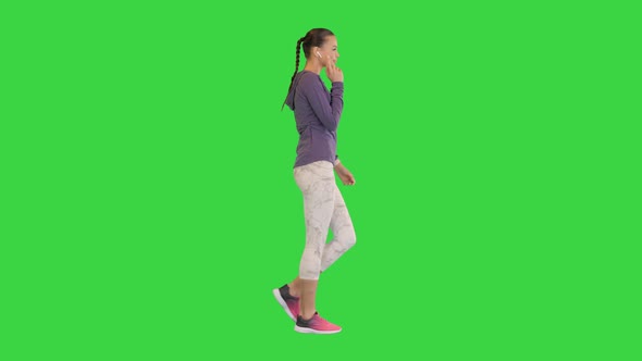Sporty Woman with Wireless Ear Buds Looking at the Screen of a Smart Watch While Walking on a Green alt