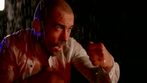 a Man in an Unbuttoned White Shirt is Boxing in Streams of Water on a Dark Background alt