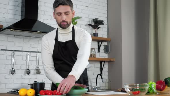 Man chef food blogger in apron prepares vegetables online video call in kitchen alt