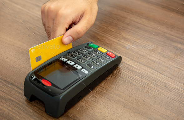 Payment machine, POS terminal and credit card isolated on wooden background.