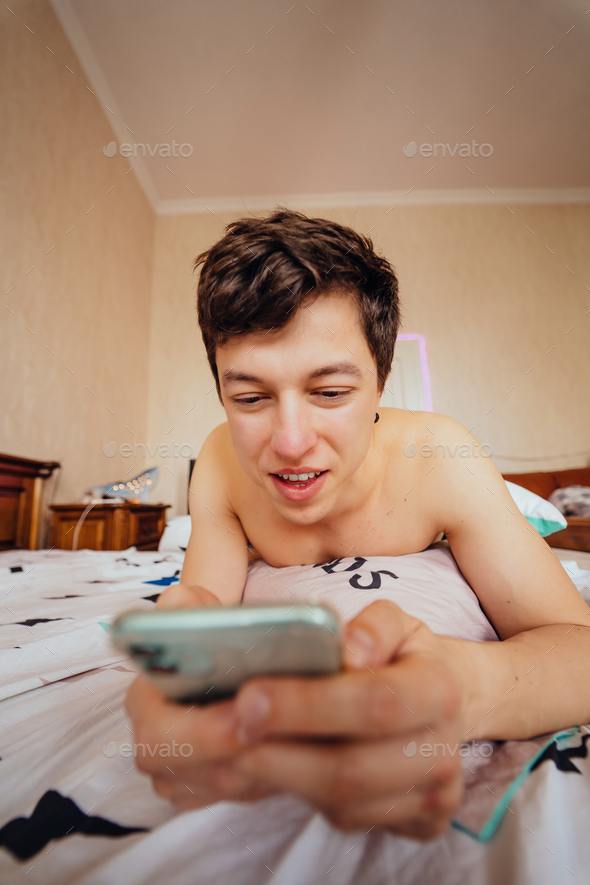 Close up shot of a guy lying in bed and using smartphone indoor