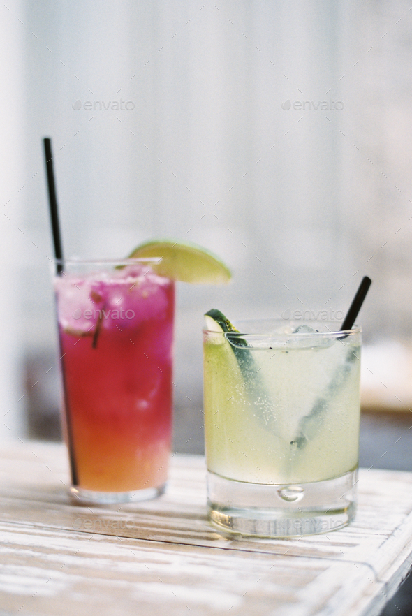 Two glasses of chilled drinks, with straws and garnishes. Lemonade and iced tea.