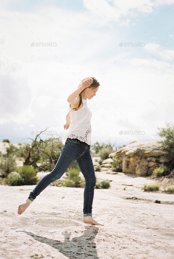 A woman wearing jeans dancing with bare feet on a rock