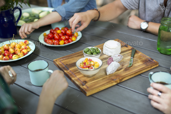 A group of people gathered around a table with plates of fresh fruits, vegetables, and cheese.