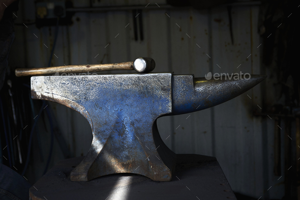 Hammer lying on an iron anvil in a traditional blacksmith\'s forge.