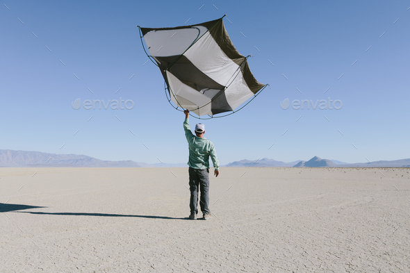 Man holding a capsule pod camping tent above his head in the open space of the desert.