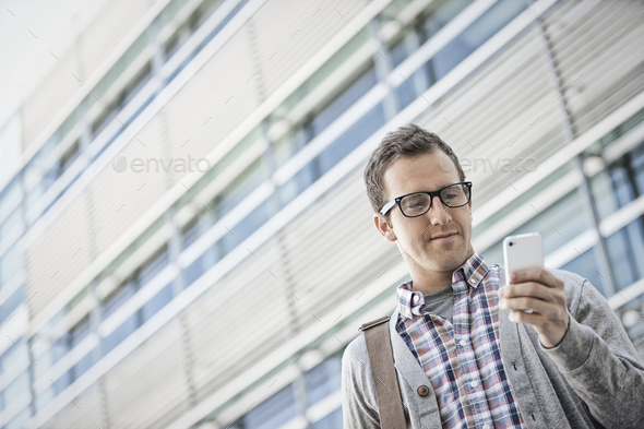 A man in a checked shirt with open collar holding his smart phone.