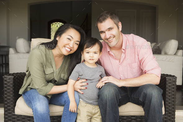 Smiling man and woman sitting side by side on a sofa, posing for a picture with their young son.