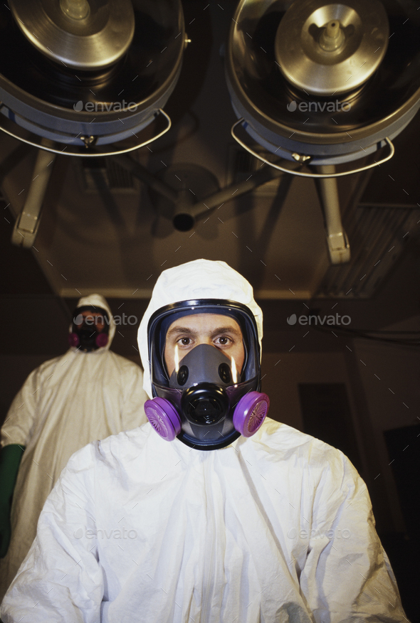 Two men wearing protective clean suits in a hospital room with lights on the ceiling.