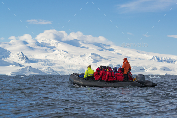 Group of people crossing the ocean in the Antarctic in a rubber boat, snow-covered mountains in the background.