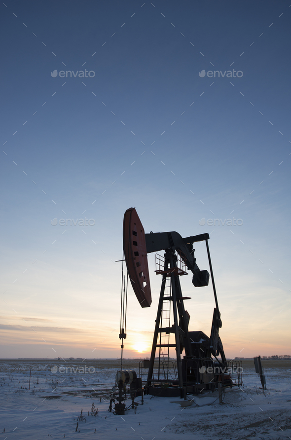 An oil drilling rig and pumpjack on a flat plain in the Canadian oil ...