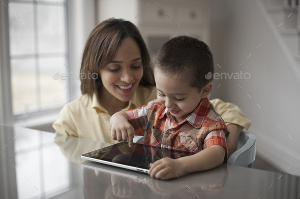 A mother and child looking at the screen of a digital tablet, the boy touching the screen.