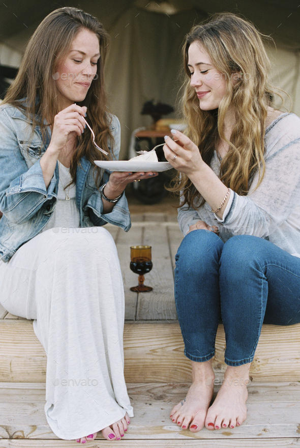 Two women sitting outdoors, sharing cake and a glass of wine.