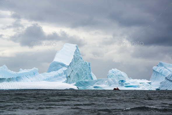 Group of people crossing the ocean in the Antarctic in a rubber boat, icebergs in the background.