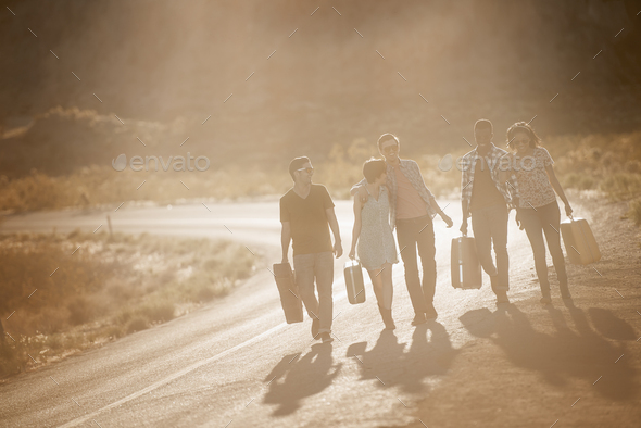A group of people, men and women, on the road with cases, in open country in the desert.