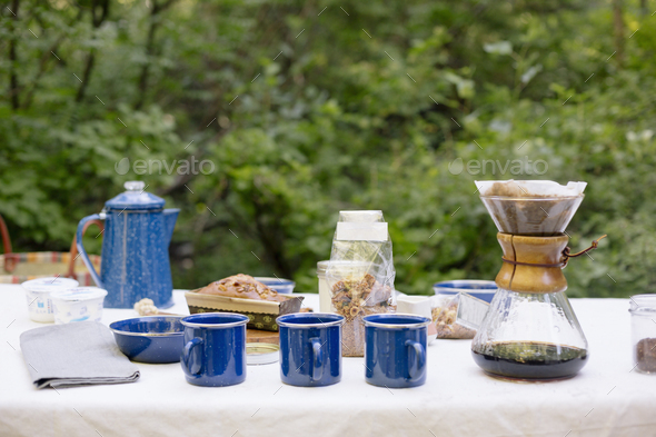 Table in a garden, with a coffee maker, mugs and bowls, a cake and cereal.