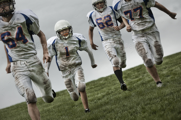 A group of four football players, young people in sports uniform and protective helmets running forward.