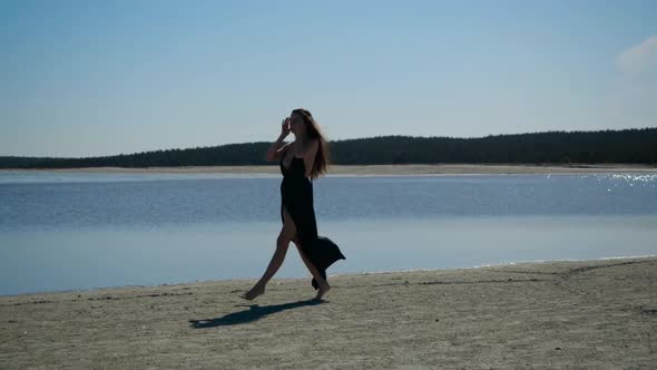 Girl Posing Walks Along the Beach in Black Dress, Wind Flutters Her Hair