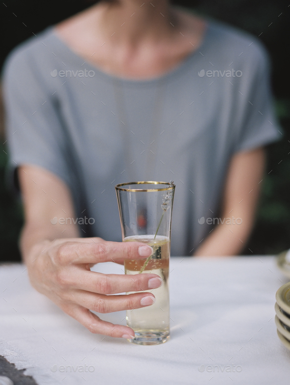 A woman holding a glass of champagne seated at a table. - Stock Photo - Images