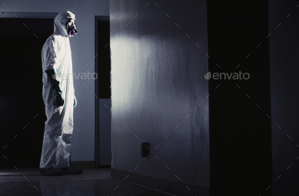 Man wearing a hazardous material protective clean suit, facing bright light in hallway