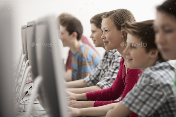 A group of young people, boys and girls, working at computer screens in class.