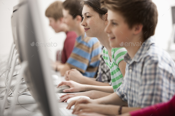 A group of young people, boys and girls, working at computer screens in class.