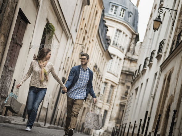 A couple walking along a narrow street in a historic city centre, with shopping bags.