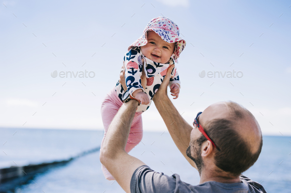 A father lifting his baby daughter in a sun bonnet up in the air,