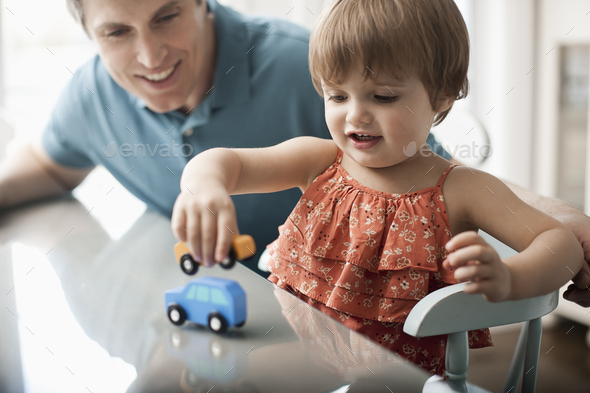 A man and a young child sitting playing with toy cars.