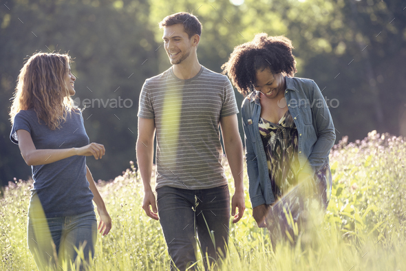 Three people, a man and two women walking through tall grass in a meadow.