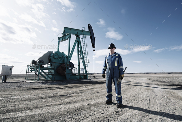 A man in overalls and a hard hat with a large wrench working at an oil extraction site.