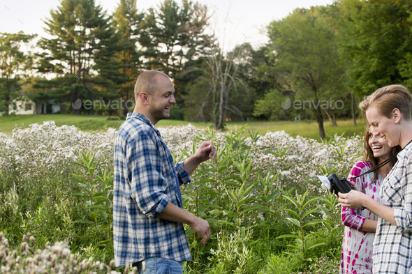 Three people, a man and two women standing in a wildflower meadow. One woman holding a camera with bulb flash attachment.