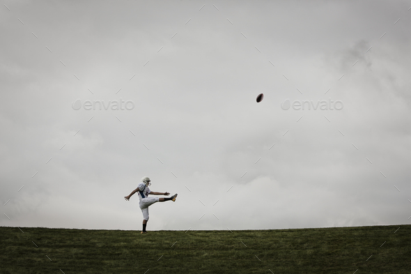 A football player in uniform, side view, practicing his kicking. Ball in mid air.