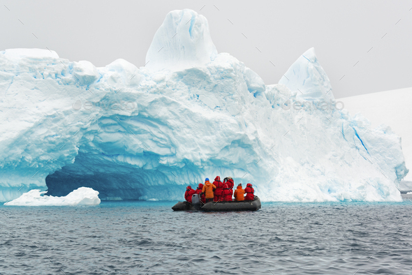 Group of people crossing the ocean in the Antarctic in a rubber boat, icebergs in the background.
