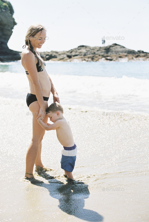 Woman in a bikini playing with her son on a sandy beach by the ocean.