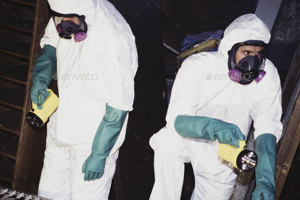 Two men wearing protective clean suits and breathing masks.