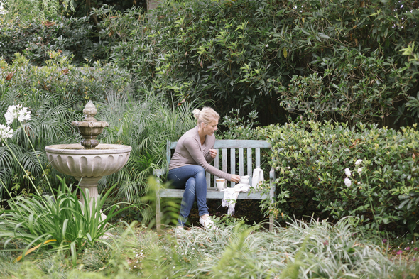 Woman sitting on a wooden bench in a garden, taking a break. - Stock Photo - Images