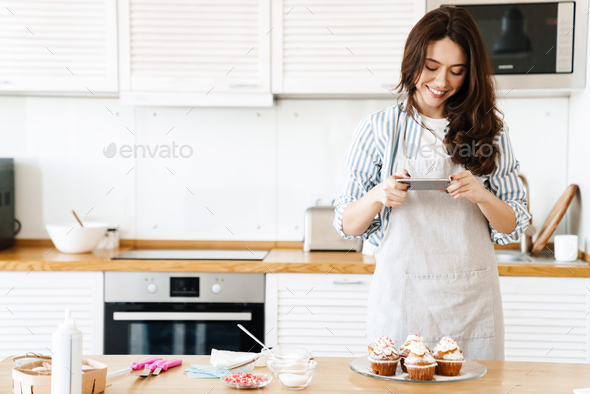 Image of caucasian smiling woman taking photo muffins on cellphone
