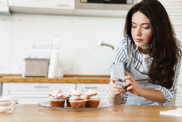 Image of caucasian concentrated woman taking photo muffins on cellphone