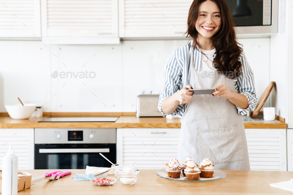 Image of caucasian smiling woman taking photo muffins on cellphone