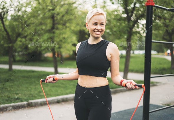 Attractive fit young woman in sport wear training with skipping rope on street workout area