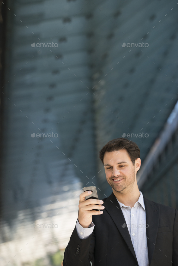 A Business man in a black jacket and open collared shirt using a smart phone.