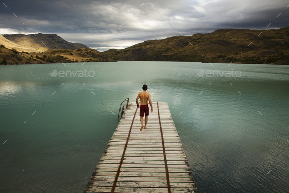 A young man walking on a wooden pier in a lake, Chile.