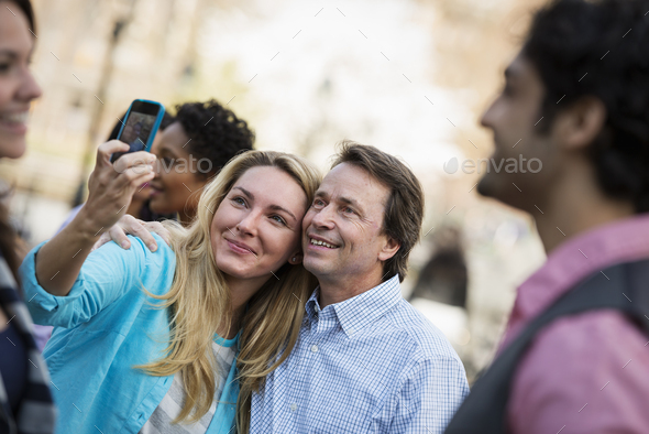 People outdoors in the city in spring time. A woman using her cell phone to take a photograph. A group of friends, men and women.